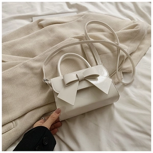 Détail d'un sac à main beige avec nœud sur un pull en maille, montrant la texture douce
