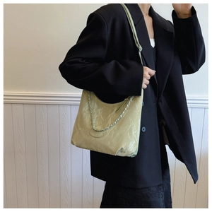 Dettaglio borsa hobo verde chiaro con tracolla a catena indossata su un blazer nero