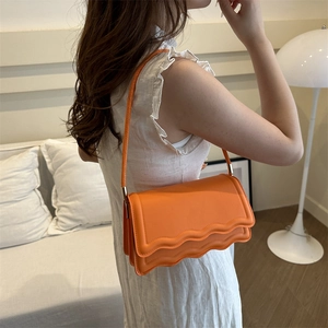 Chic orange crossbody bag featuring a unique wavy edge design and gold metal hardware