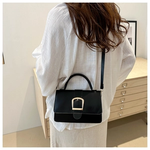 Détail d'un sac bandoulière noir avec boucle en U dorée porté par un mannequin femme