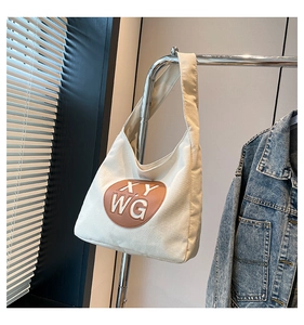 Detail of off-white canvas tote bag with brown round leather logo patch on a metal hanger