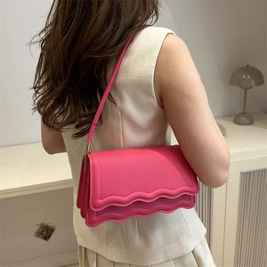 Pink crossbody square bag with wavy flap design and slim shoulder strap shown on model