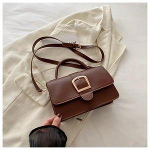 Détail d'un sac bandoulière en similicuir marron mat avec boucle dorée sur un blazer beige