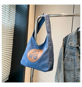 Detail view of denim canvas tote bag with brown leather XYWG patch on a metal hanger
