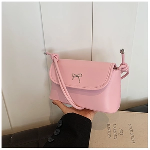 Detail of light pink crossbody bag featuring a silver metal bow and knotted rope strap