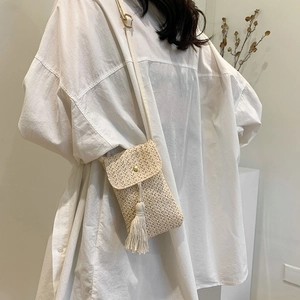 Straw mini crossbody bag with tassels and gold buckle on a minimalist model shot