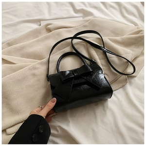 Détail d'un sac bandoulière en cuir verni noir avec un nœud décoratif et une finition brillante