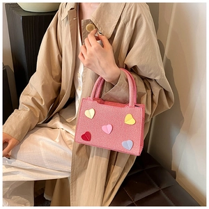 Petit sac carré rose avec écussons cœurs colorés porté par un mannequin en trench-coat