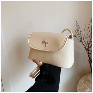 Close-up of beige crossbody bag with gold bow clasp and sleek leather shoulder strap