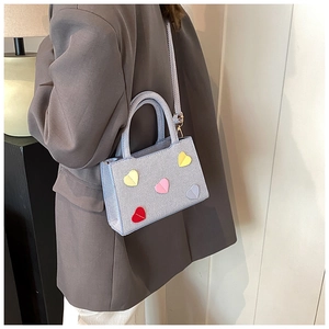 Détail d'un mini sac à main bleu clair avec des patchs cœurs colorés et boucles métalliques