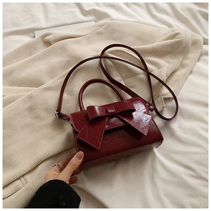 Détail d'un mini sac bordeaux à nœud en cuir brillant sur fond de blazer clair