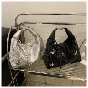 Détail de sacs fourre-tout plissés avec breloques papillon argentées sur étagère en verre