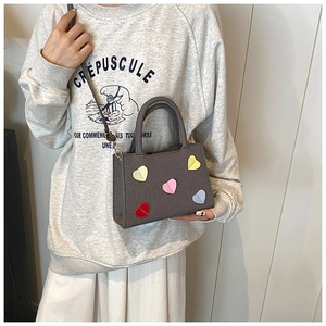 Détail du sac bandoulière gris texturé avec écussons cœurs colorés et fine bandoulière