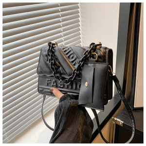 Close-up of black quilted leather bag with FASHION embossing and chain detail