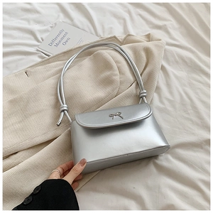 Detail of silver metallic handbag with bow ornament and stylish cylindrical handle
