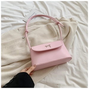 Close-up of pink shoulder bag featuring a silver metal bow and textured matte leather