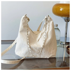 Dettaglio borsa hobo bianca con texture in pelle plissettata e catena su tavolo di vetro