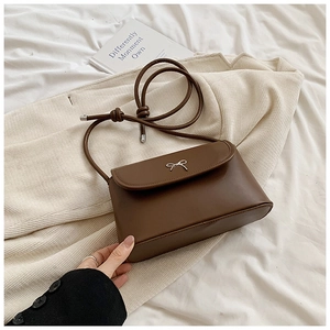 Detail of dark brown leather shoulder bag featuring a silver bow metal decoration