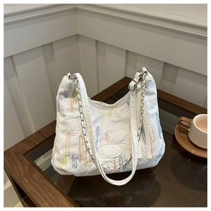 Detail of colorful embroidery textures and silver chain strap on a white quilted tote bag