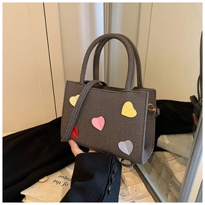 Détail du sac à bandoulière gris texturé avec écussons en cuir cœur 3D et boucle dorée chic