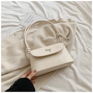 Detail of creamy white shoulder bag featuring a metallic bow buckle and knotted strap