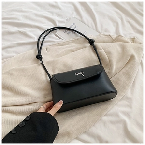 Detailed macro of a black matte leather bag featuring a silver metal bow buckle accent