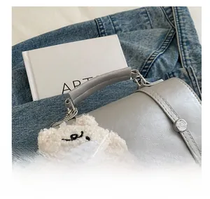 Detail of light grey leather handbag with plush bear charm and embroidery detail