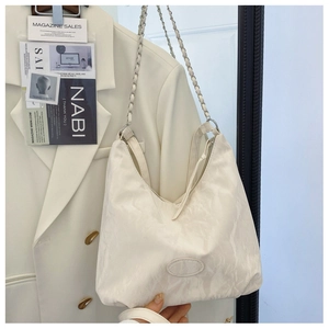 Dettaglio borsa a spalla bianca in pelle testurizzata con catena argento e zip su blazer
