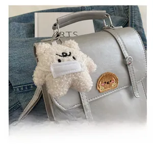 Close-up of a white plush bear charm with mask attached to a grey leather shoulder bag