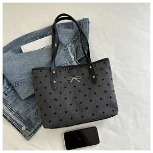 Close-up of grey polka dot tote bag with silver metal bow and black leather handles