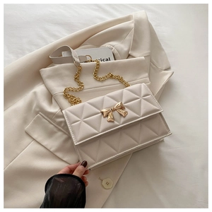Dettaglio della borsa trapuntata bianco crema con chiusura a fiocco dorato su blazer