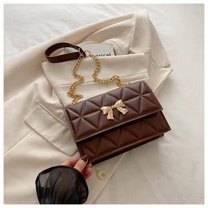 Dettaglio borsa trapuntata marrone scuro con chiusura a fiocco dorata su blazer beige