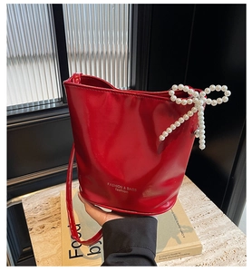 Detailed macro view of the glossy red bucket bag featuring a pearl bow and silver bell charm