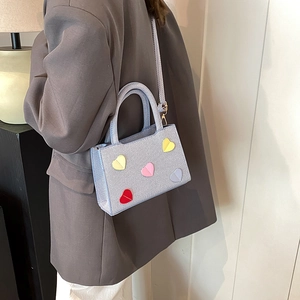 Sac à main carré bleu clair avec patchs cœurs colorés porté par un mannequin chic