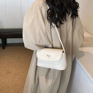 Creamy beige leather crossbody bag with silver bow accent worn with khaki coat