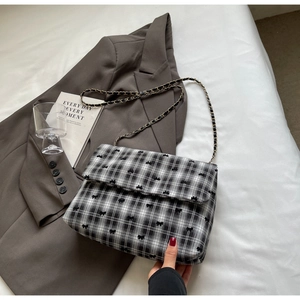 Détail du sac à carreaux noir et blanc avec nœuds imprimés et bandoulière en chaîne