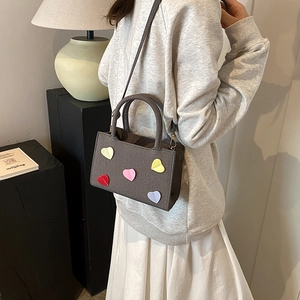 Sac bandoulière gris texturé avec patchs cœurs colorés et poignée tressée, vue de côté