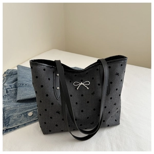 Close-up of polka dot pattern and silver bow charm on a dark grey canvas tote bag