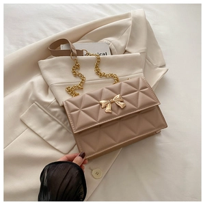 Dettaglio borsa a tracolla trapuntata beige con fibbia a fiocco dorato e catena