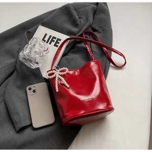 Detail of red glossy bucket bag with pearl bow charm on a grey suit background