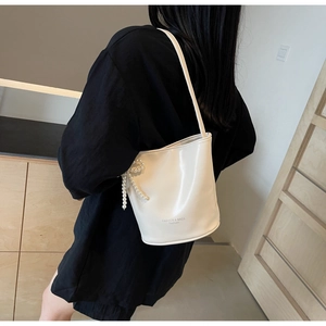 Detail view of a white bucket bag featuring a pearl bow pendant and sleek finish