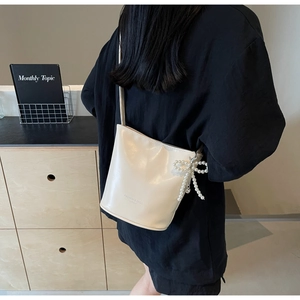 Close-up of cream leather bucket bag featuring a pearl bow charm and logo detail
