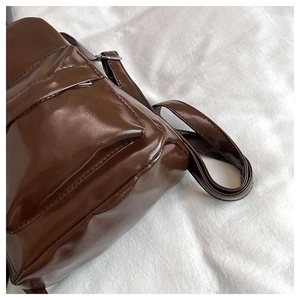 Detail of glossy brown faux leather texture and silver buckle on a stylish backpack