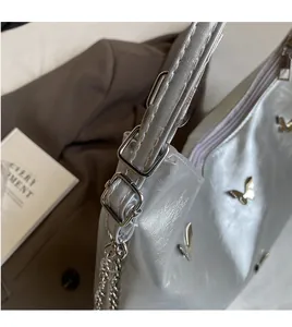 Detail of silver metallic tote bag featuring butterfly ornament and adjustable shoulder strap