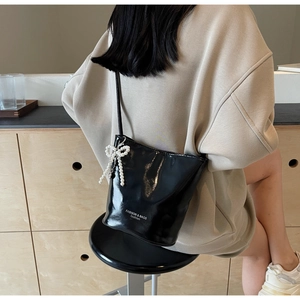 Glossy black bucket bag with a decorative pearl bow charm shown on a female model