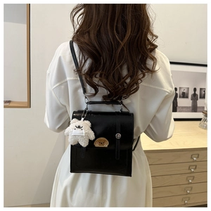 Detail of black glossy leather backpack with cute puppy embroidery and plush bear charm