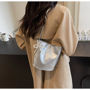 Silver glossy bucket bag with pearl bow decoration worn over a trench coat