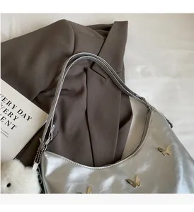 Silver tote bag with metal butterfly details and a white fluffy charm on a magazine