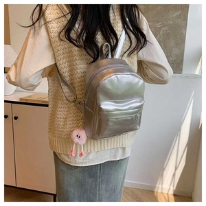Detail of silver metallic PU mini backpack with a pink plush charm on model back