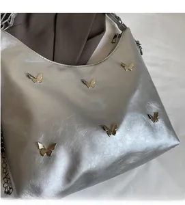 Detailed view of silver metallic bag with 3D butterfly charms and zip closure